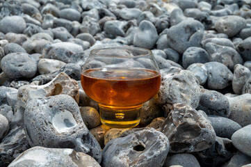 Glass of apple cider drink and stones on pebbles beach of Etretat, Normandy, France