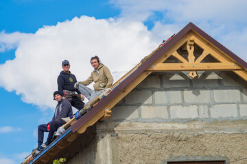 three Roofer man roof carpenter working Country house renovation. looking at camera blue sky beautiful clouds, unfinished wall  concrete block