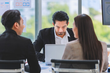 Millennial Asian professional successful bearded businessman in formal suit brainstorming discussing talking with unrecognizable unknown male and female colleagues in company office meeting room.