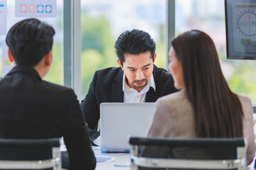 Millennial Asian professional successful bearded businessman in formal suit brainstorming discussing talking with unrecognizable unknown male and female colleagues in company office meeting room.