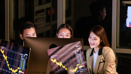 Asian professional successful female businesswoman trader investor mentor in formal suit sitting helping supporting male female colleague intern trainee working with investing data at night.