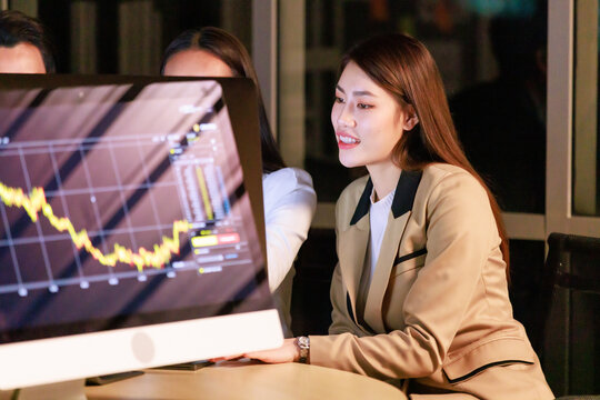 Asian Professional Successful Female Businesswoman Trader Investor Mentor In Formal Suit Sitting Helping Supporting Male Female Colleague Intern Trainee Working With Investing Data At Night.