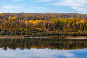 Beautiful, wide autumn river among forests and rocky shore. A calm and quiet place with autumn colors. Reflection of clouds in the water in good weather