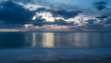 Obraz premium Evening twilight over the Indian Ocean. Blue clouds in the sky, highlighted in pink. Reflection on turquoise water. Foam of waves on the sand of the beach. Long exposure. Seychelles. Mahe. Beau Vallon