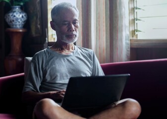 Fototapeta premium senior man reading news on laptop Asian mature man using a laptop at home