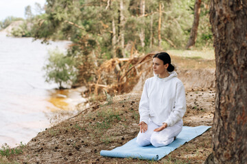 Beautiful european woman doing breathing yoga exercise in the park, European female meditation pose, healthcare.