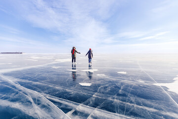 Winter lake Baikal Russia, two tourist women friends in red cap are skating on ice frozen, sunny day