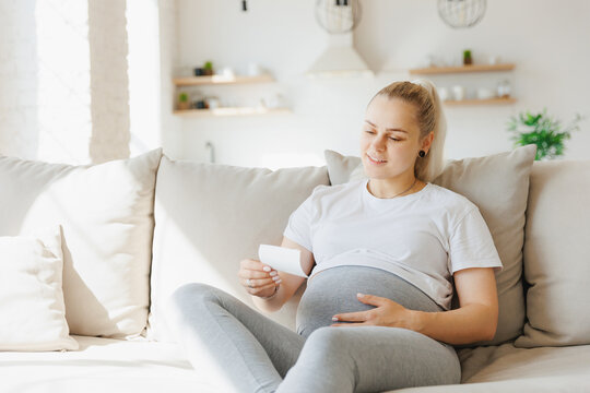 Pregnant woman with ultrasound image on sofa. Concept expectant mother waiting for baby birth during pregnancy, light background