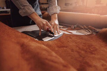 Cobbler Man tailor cuts out blanks for sewing bags or shoes according to pattern made of leather