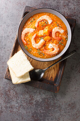 Pumpkin puree soup with shrimp, sesame and thyme served with bread on a wooden tray on the table. Vertical top view from above