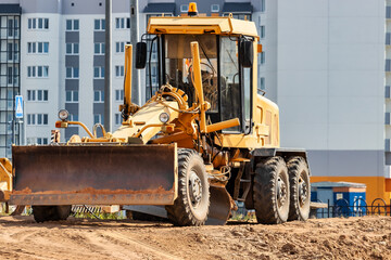Road grader at the construction site. Powerful construction machine for ground leveling and excavation. Close-up. Professional construction equipment.
