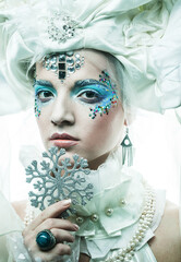 Young beautiful woman with creative make-up in a New Year's style holds a silver snowflakes near her face.