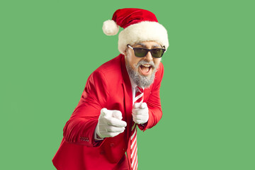 Fototapeta na wymiar Hey you. Happy funny confident positive man with beard and handlebar mustache in funky red suit, tie, Christmas Santa cap, white gloves and cool sunglasses points index finger at you. Studio portrait