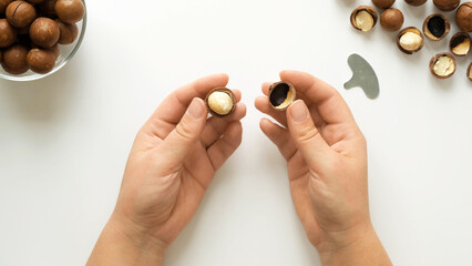 Opening a macadamia nut with a metal key. Female hands show a opened nut on a white background top view