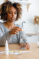 African American woman with a cold and headache drinks soluble cough pills and antipyretics. A tired sick woman at home takes pills for fever and sore throat or vitamins.