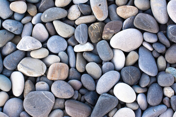 Background with round pebble stones. Stones beach smooth, flat lay texture in daylight. Top view. Summer day.