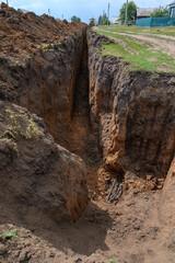 A narrow and deep trench in clay soil in the countryside. The process of laying engineering water supply systems.