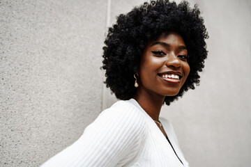 Black woman with afro hair posing in front of a gray concrete wall