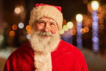 Portrait of kind Santa Claus looking at camera and smiling in night city setting
