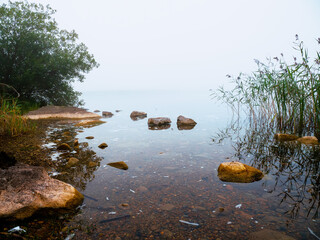 Warm orange color rocks in a river or lake and cool fog in the background. Calm water surface. Beautiful nature scene. Nobody, selective focus. Warm and cool tone. Misty weather