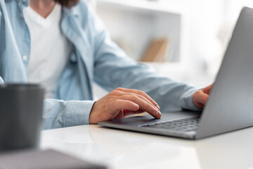 Close up shot of a man sitting at the table and working on laptop at home