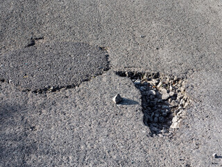 Two pot holes on a road side by side. One fixed other in need of repair. Road surface poor quality...