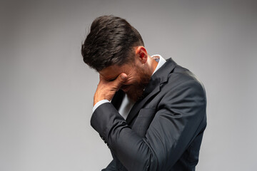 Guilty cringing businessman closes face with palm on gray background