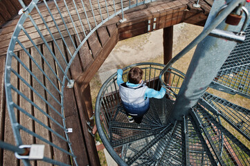 Boy walk at spiral staircase on wooden observation tower.