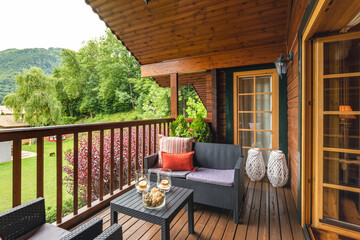 Cozy terrace with table and sofa at wooden cottage house surrounded by greenery and trees in...
