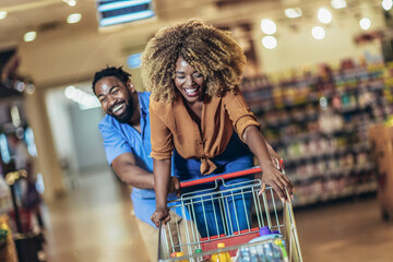 African American couple with trolley purchasing groceries at mall, having fun.