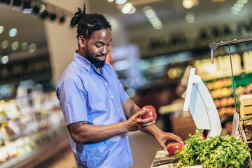 African American man is measuring fruits and vegetables on digital scale for customers.