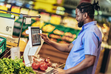 African American man is measuring fruits and vegetables on digital scale for customers.