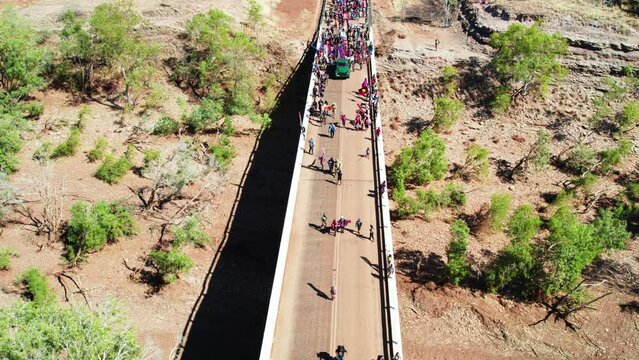 Aerial View Of Children Leading Crowds Over The Bridge Across The Victoria River In The Freedom Day Festival March In The Remote Community Of Kalkaringi, Northern Territory, Australia. 26 August, 2022