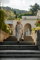 Woman on the stairs in the park. A middle-aged lady in a hat in a white outfit with a bag walks around the Livadia Palace