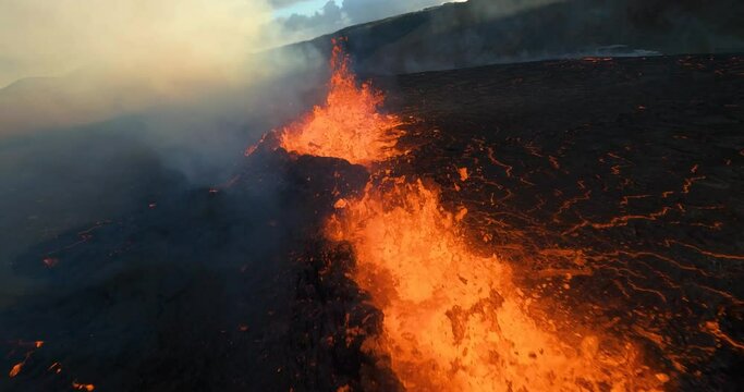 FPV drone shot closely over erupting craters and a glowing lava field - slow motion view