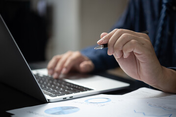 Hand holding pen document graph and chart report finance investment marketing and business accounting analysis plan growth information with computer laptop on desk.