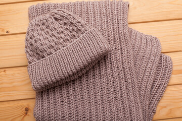 knitted scarf and woolen hat women's winter set in beige tones on a wooden background.