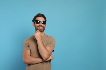 Fototapeta premium Portrait of smiling bearded man with stylish sunglasses on light blue background. Space for text