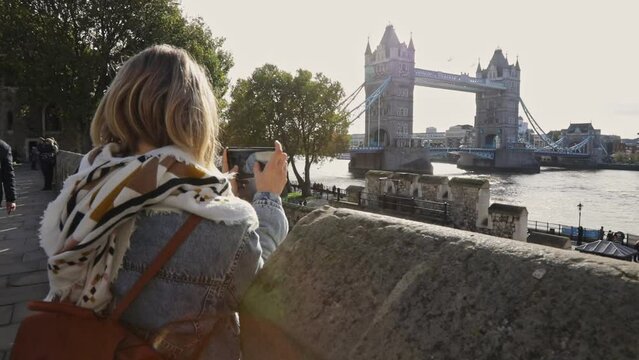 Young woman taking a photo with her smartphone of Tower Bridge and Thames River in London England on a sunny winter day