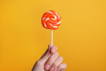 Woman holding bright tasty lollipop on orange background, closeup