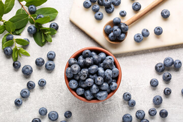 Tasty fresh blueberries and green leaves on light grey table, flat lay