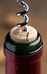 Opening wine bottle with corkscrew on blurred background, closeup