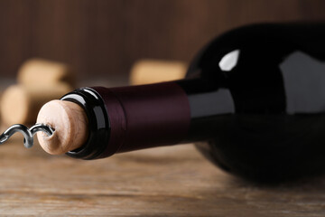 Opening wine bottle with corkscrew on wooden table, closeup