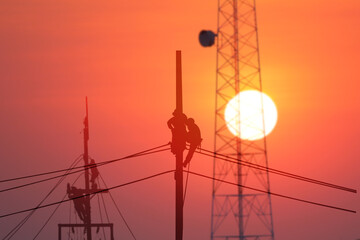 electrician working over load on pole with telecommunication pole whie sun set nature background