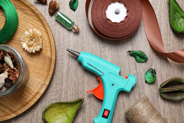 Hot glue gun and handicraft materials on wooden table, flat lay