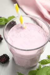 Delicious blackberry smoothie in glass with straw on white table, closeup
