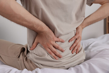 Fototapeta na wymiar Man suffering from back pain while sitting on bed indoors, closeup. Symptom of scoliosis