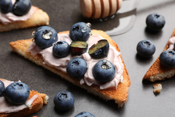 Tasty sandwiches with cream cheese, honey and berries on grey table, closeup