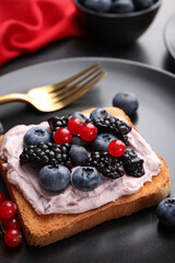 Tasty sandwiches with cream cheese and berries on black plate, closeup