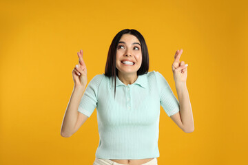 Woman with crossed fingers on yellow background. Superstition concept - obrazy, fototapety, plakaty